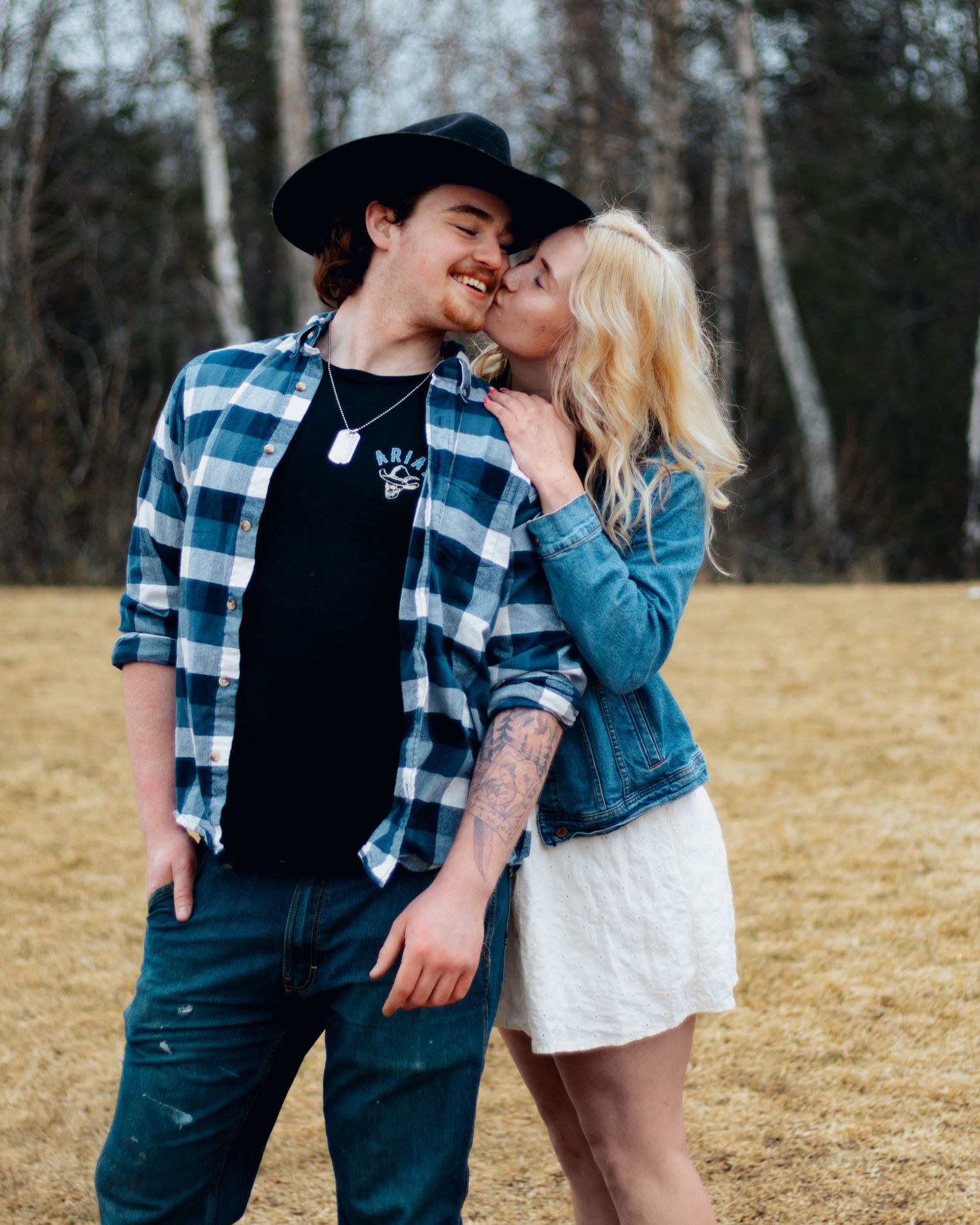 A young couple shares a tender kiss outdoors, with the woman in a denim jacket and white skirt.