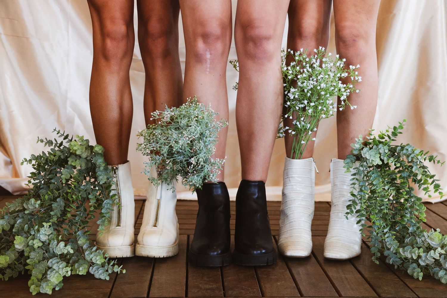 Four people standing in a row showing legs and ankles wearing white and black boots with floral bouquets.