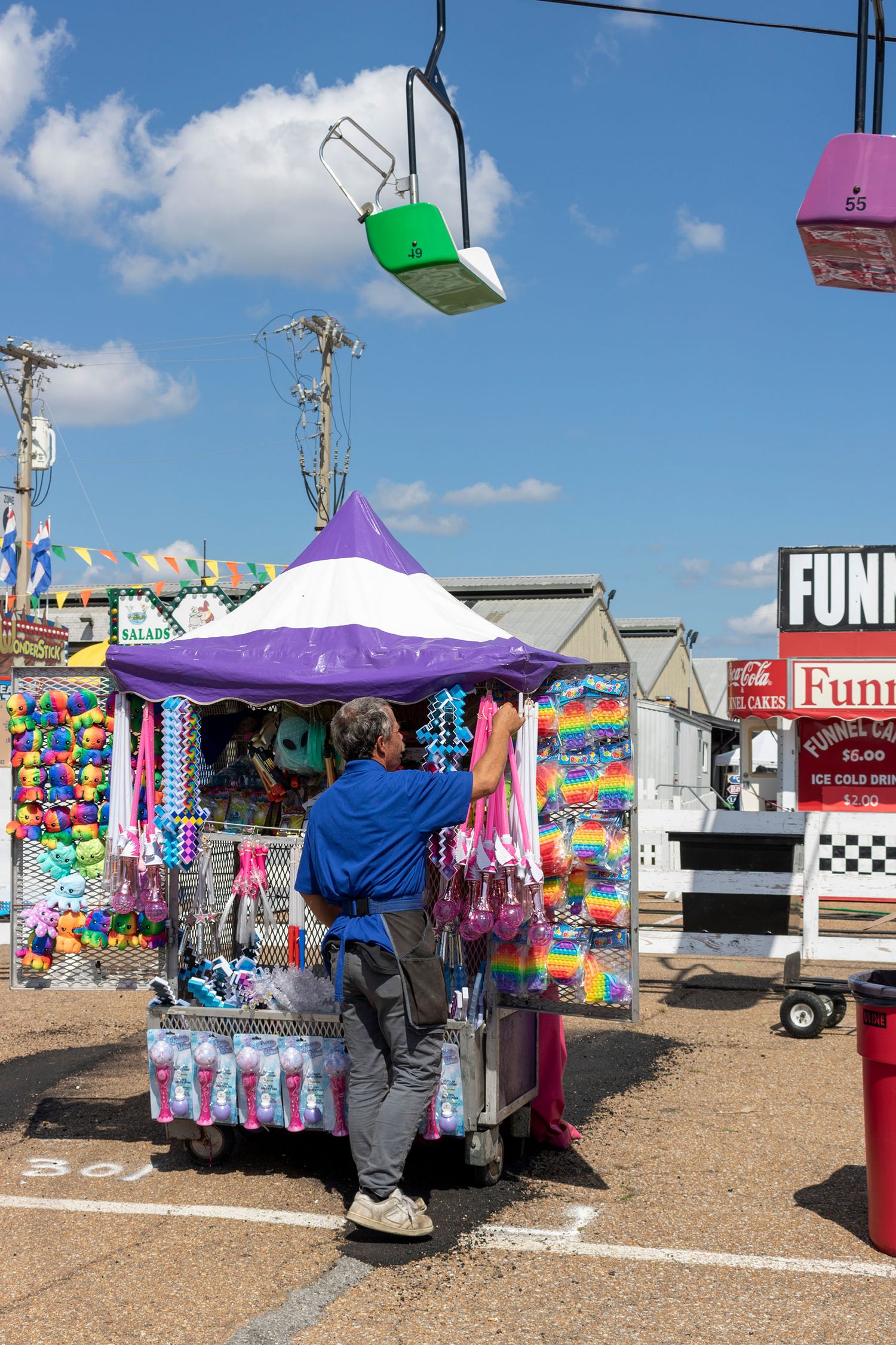 A colorful carnival game booth with a purple tent and hanging prizes at an outdoor state fair.