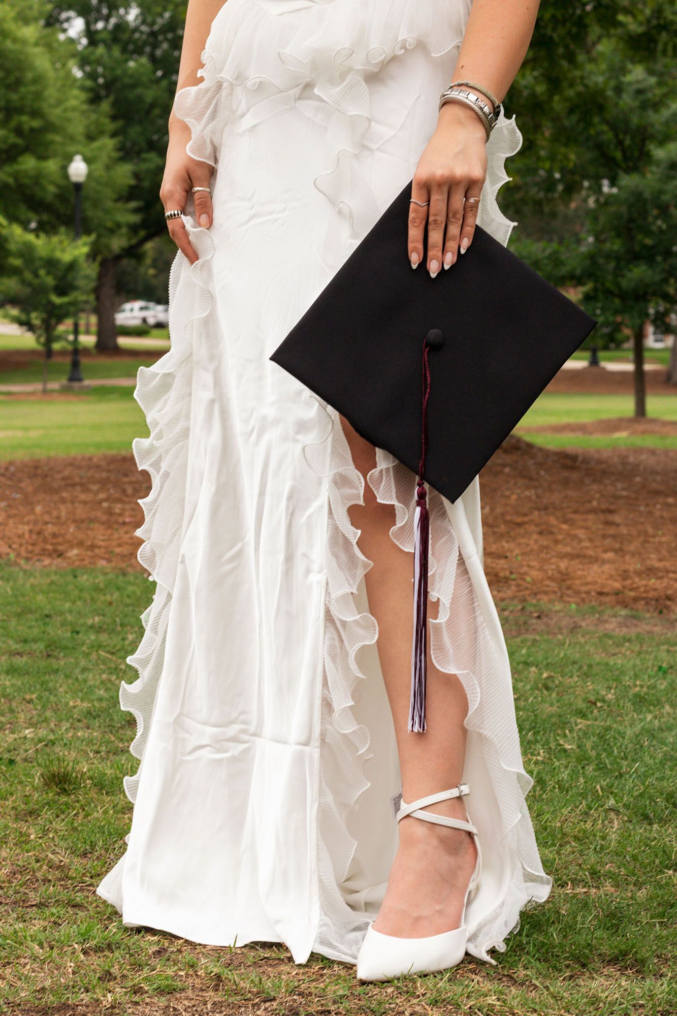 Close-up of graduate in white ruffled dress holding black graduation cap with tassel.