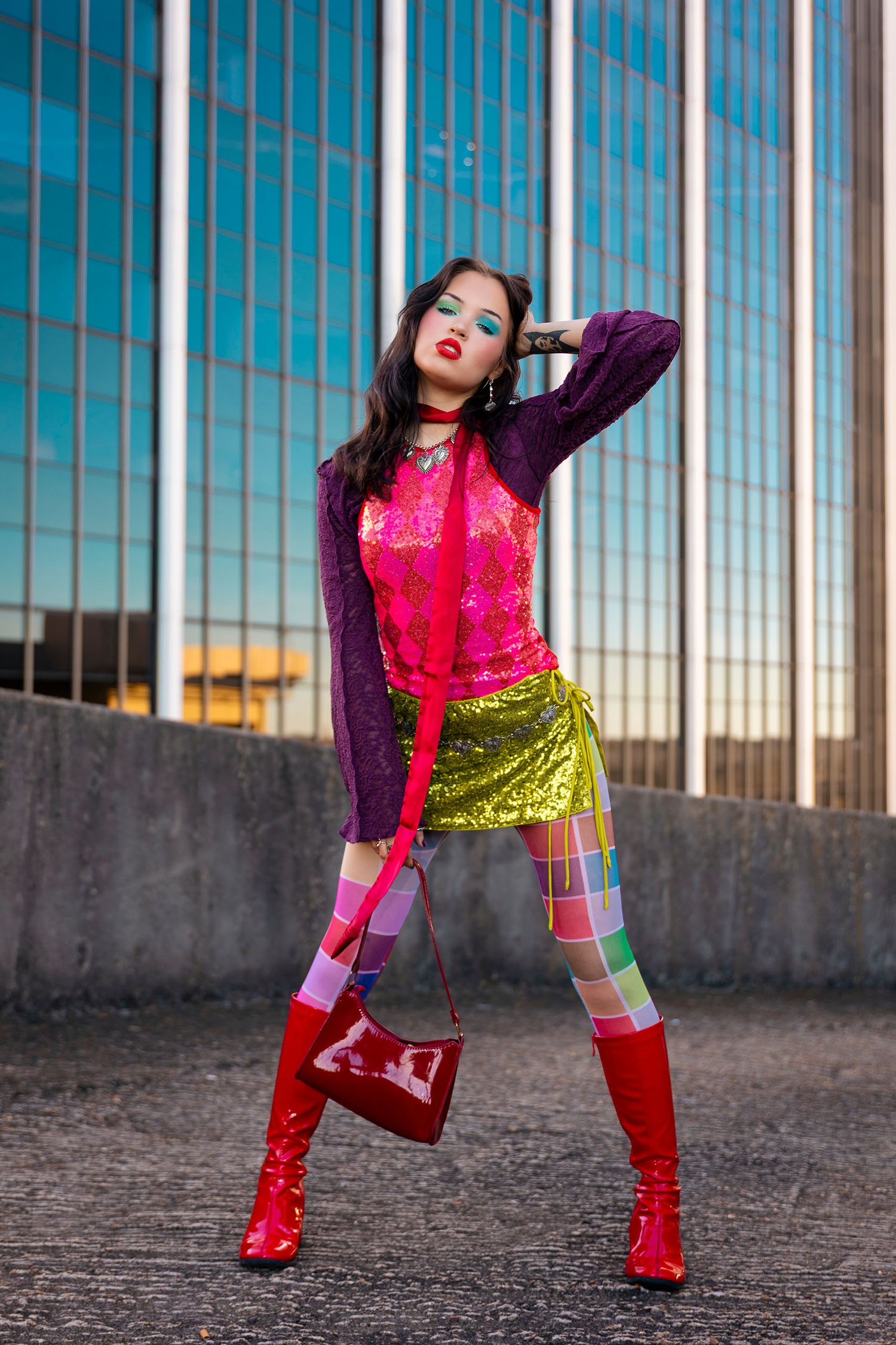 Bold fashion model in pink sequin top, green skirt, plaid tights, and red knee-high boots outdoors.