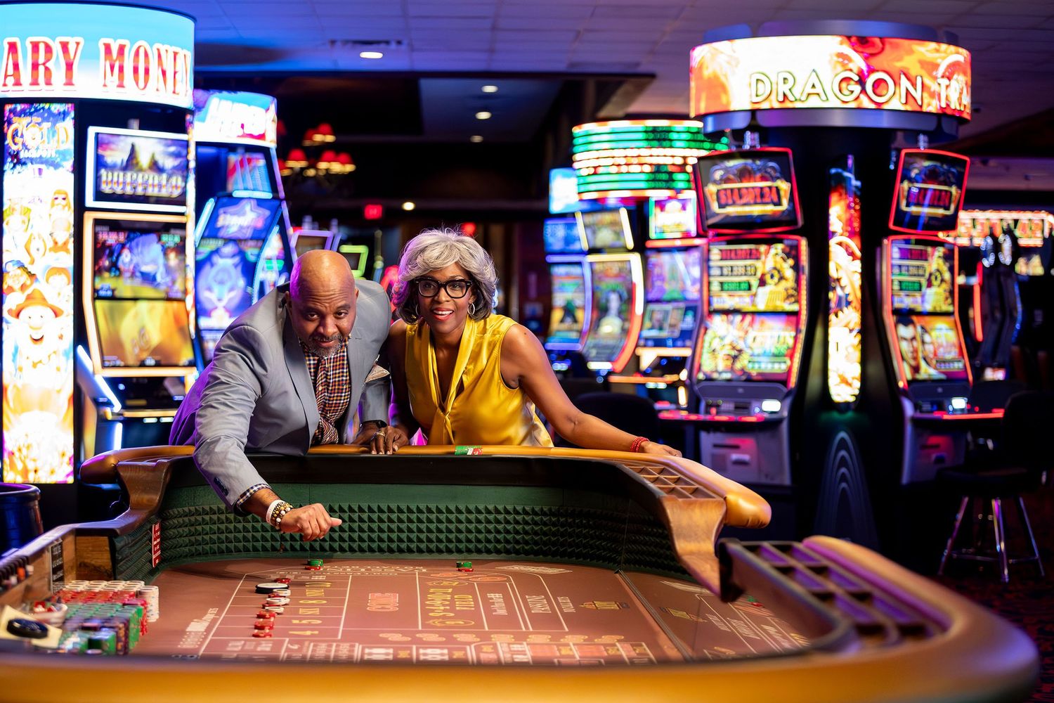 Couple enjoying a craps table at a vibrant casino filled with colorful slot machines.