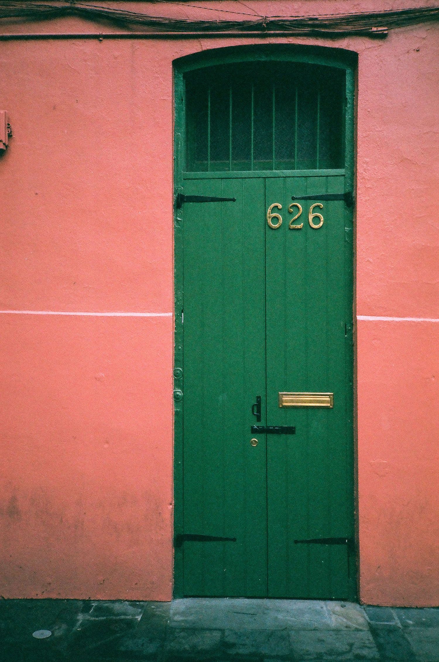 A green wooden door numbered 626 set against a pink stucco wall in New Orleans French Quarter.