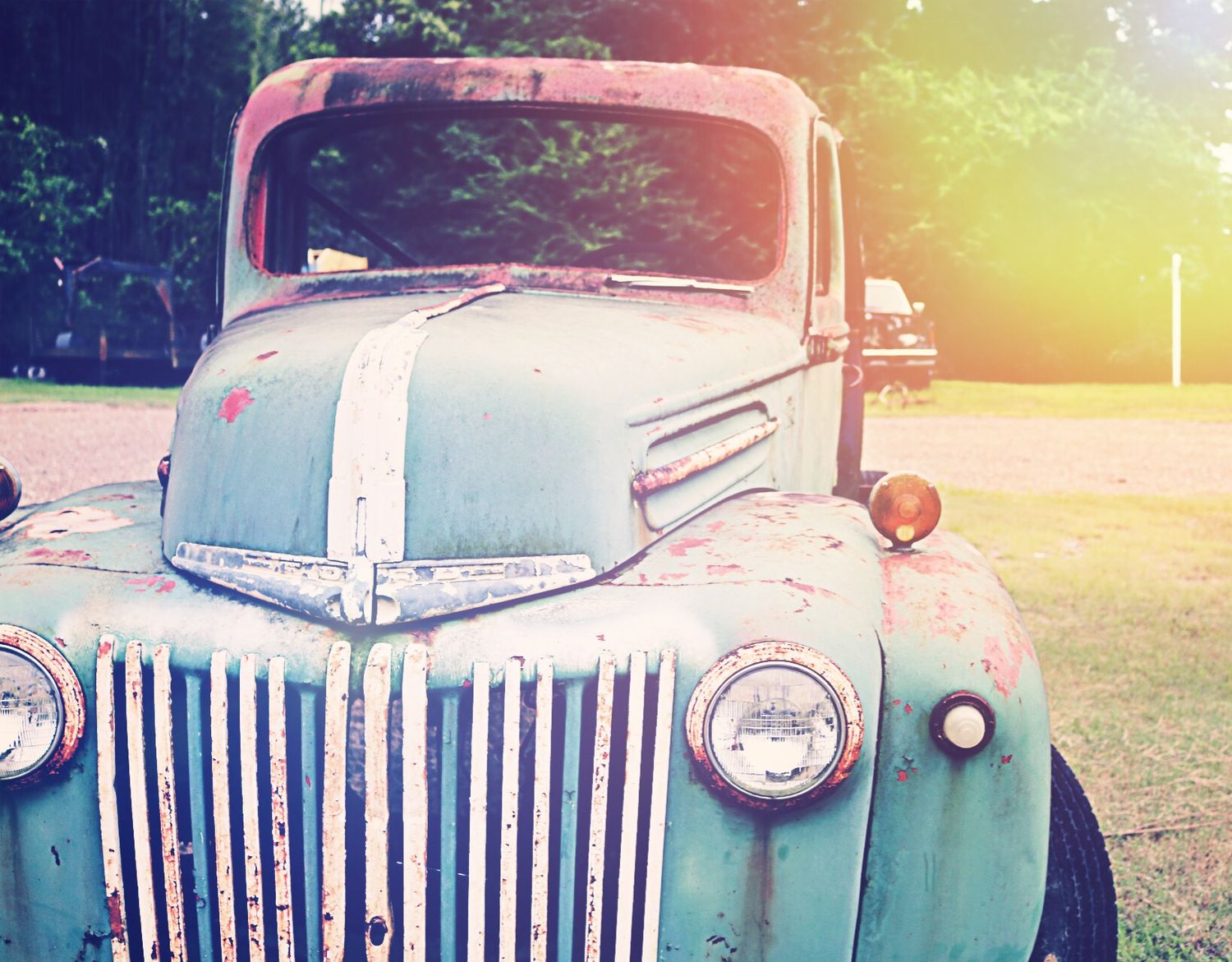 A vintage rusty turquoise Ford truck parked outdoors with a warm golden sunlight lens flare effect.