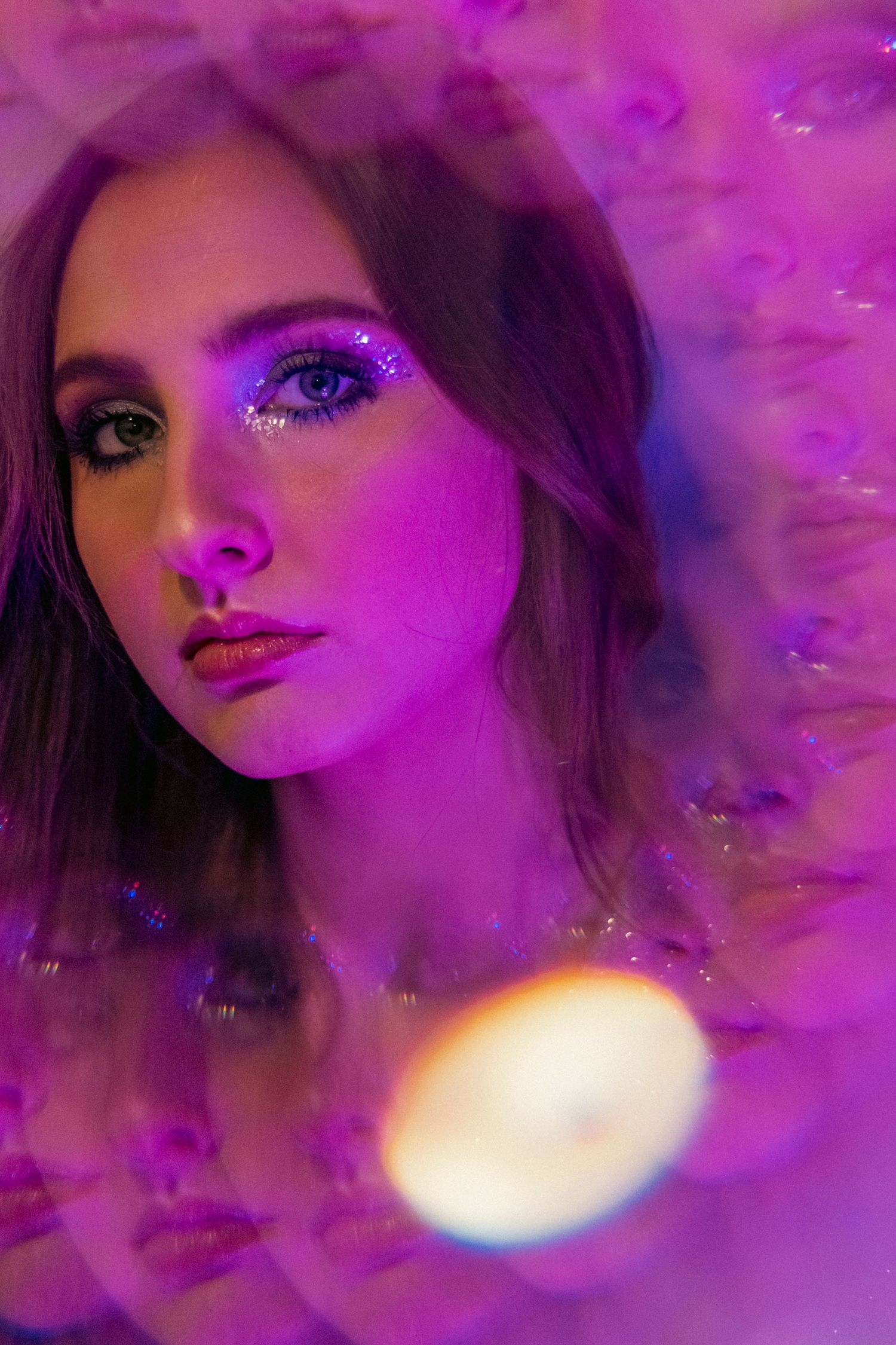 Close-up portrait of woman with glitter eye makeup in purple neon light with dreamy bokeh effect.
