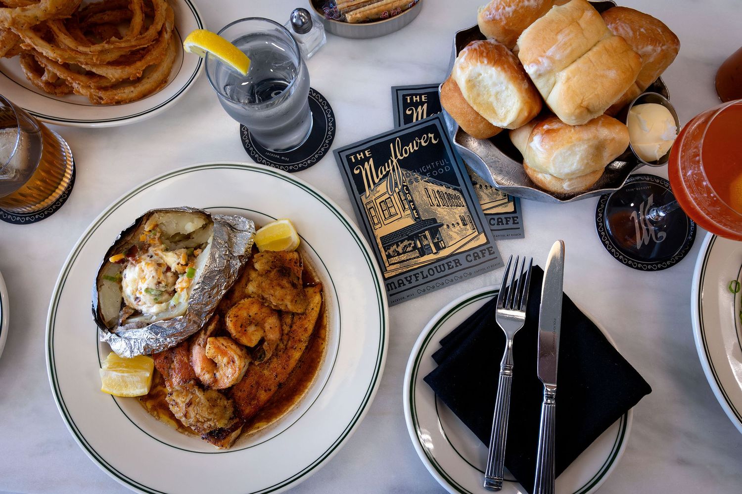 Close-up of a plated fish and shrimp entree with rolls and cocktail on a white tablecloth.