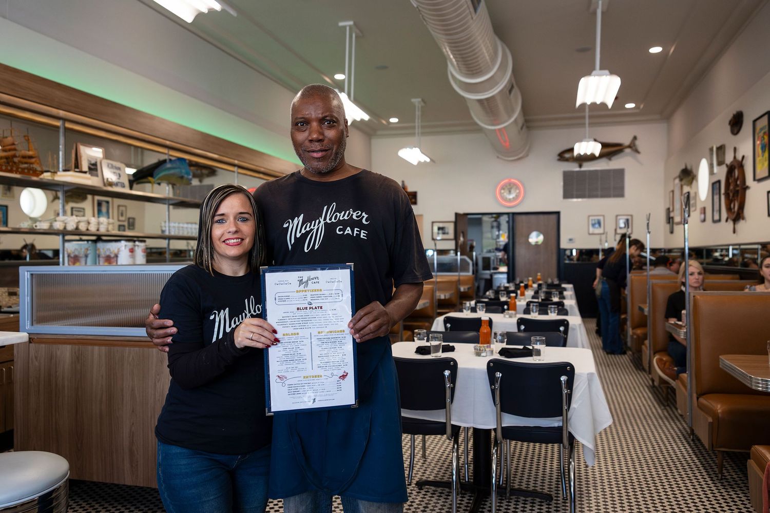 Two staff members proudly display a certificate inside the bright and classic May flower Cafe diner.