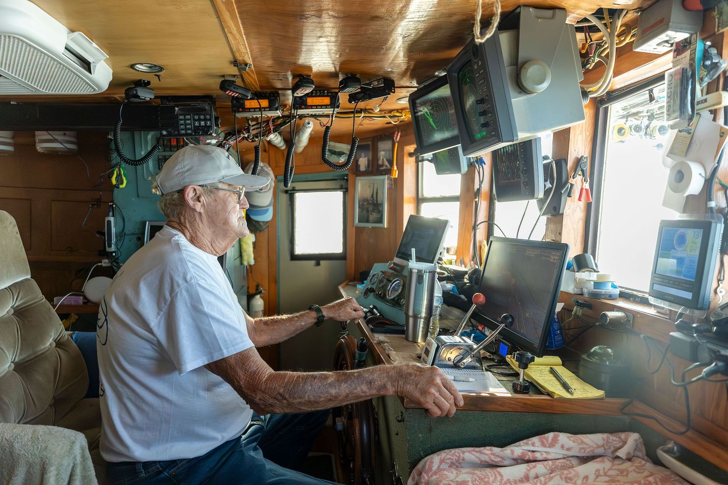 Elderly boat captain operating navigation equipment in a cluttered wheelhouse.
