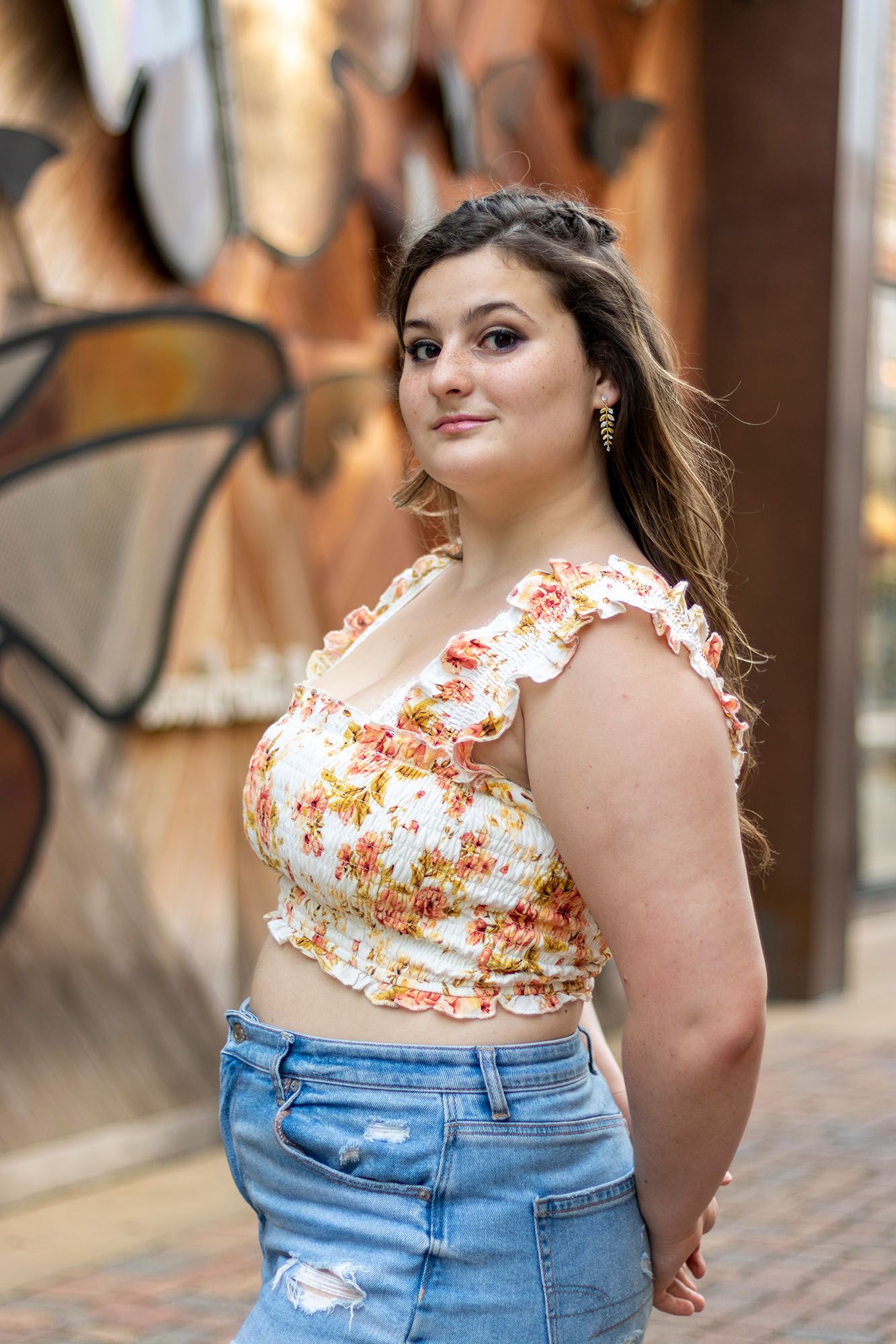 Confident plus-size young woman in floral crop top and denim skirt posing near graffiti wall.