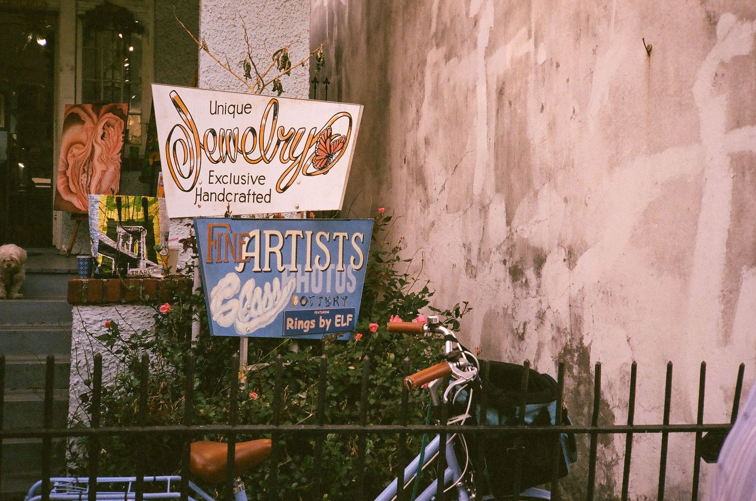 Colorful handmade jewelry and artists signs displayed outside a shop with a bicycle parked nearby.