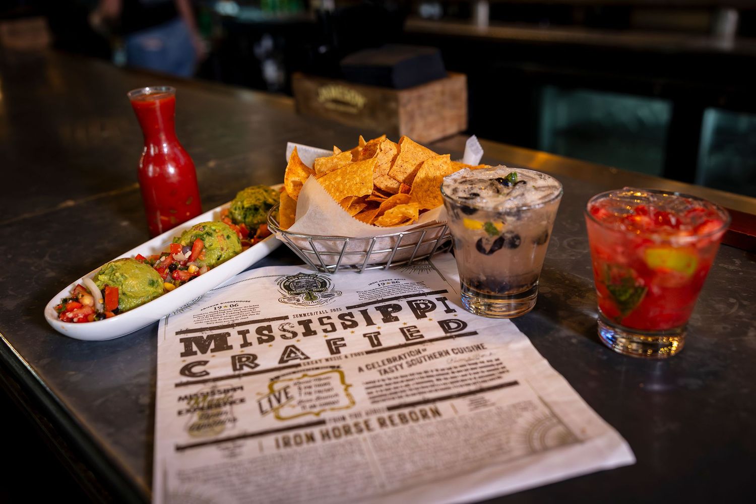 Mississippi Crafted menu displayed with chips, dips, and cocktails on a bar table.