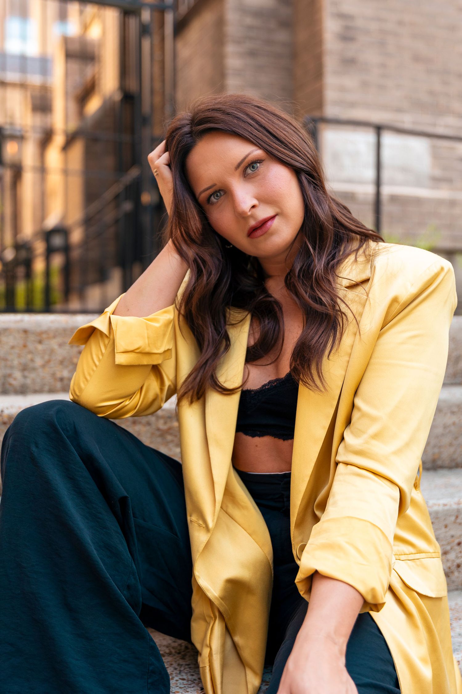 Woman in yellow blazer and black crop top sitting on steps in urban setting.