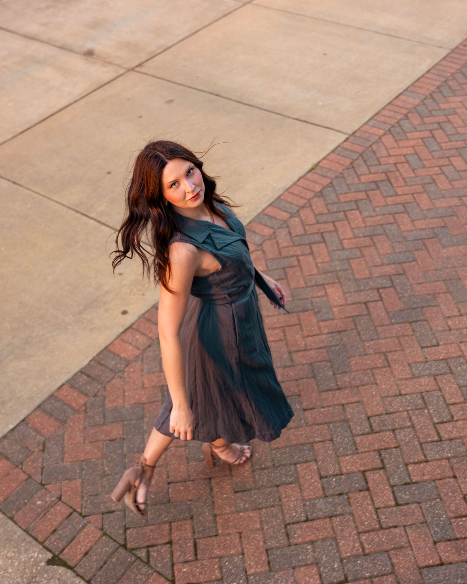 Aerial view of woman in teal pleated dress standing on brick pavement outdoors.