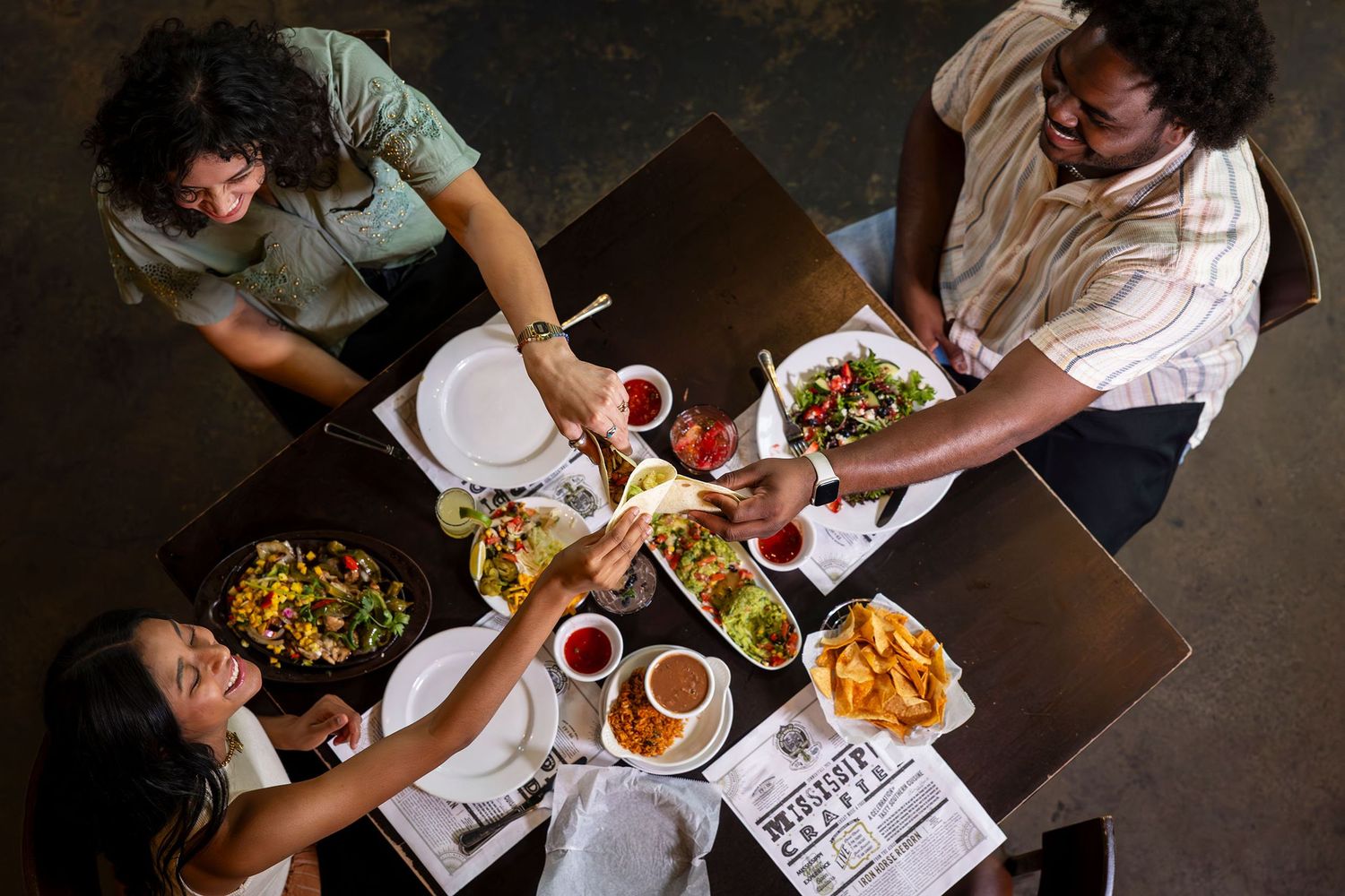 Overhead view of four friends toasting and sharing food at a restaurant table.