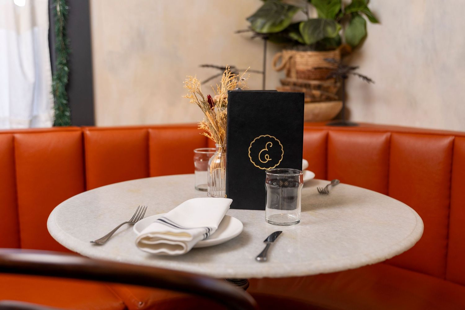 Elegant restaurant table setting with orange booth, marble table, and black menu.