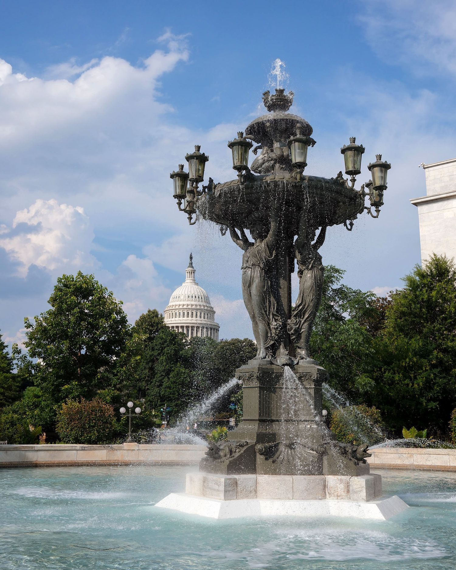 Ornate Bartholdi Fountain with US Capitol dome visible through trees under blue sky.