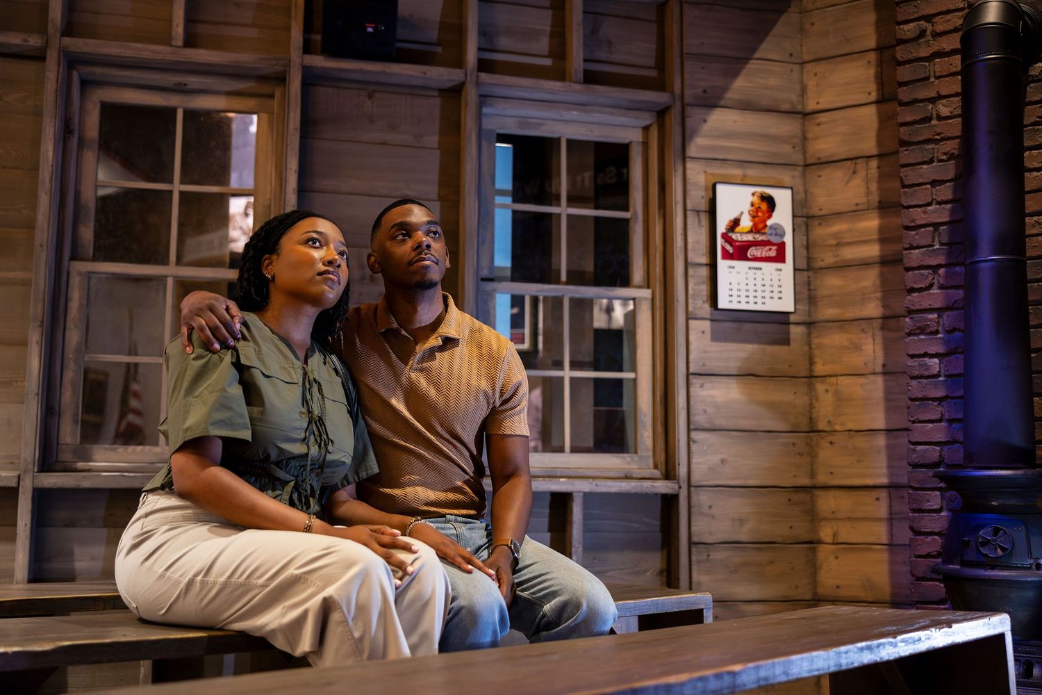 Two actors sit together on a rustic porch in a dramatic theater stage production scene.