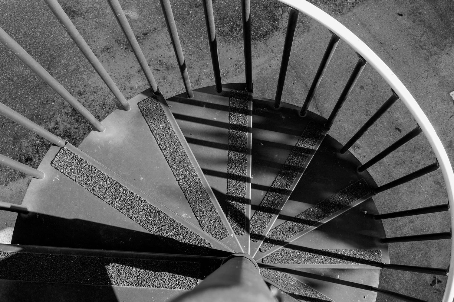 Aerial black and white view looking down a metal spiral staircase with geometric shadow patterns.