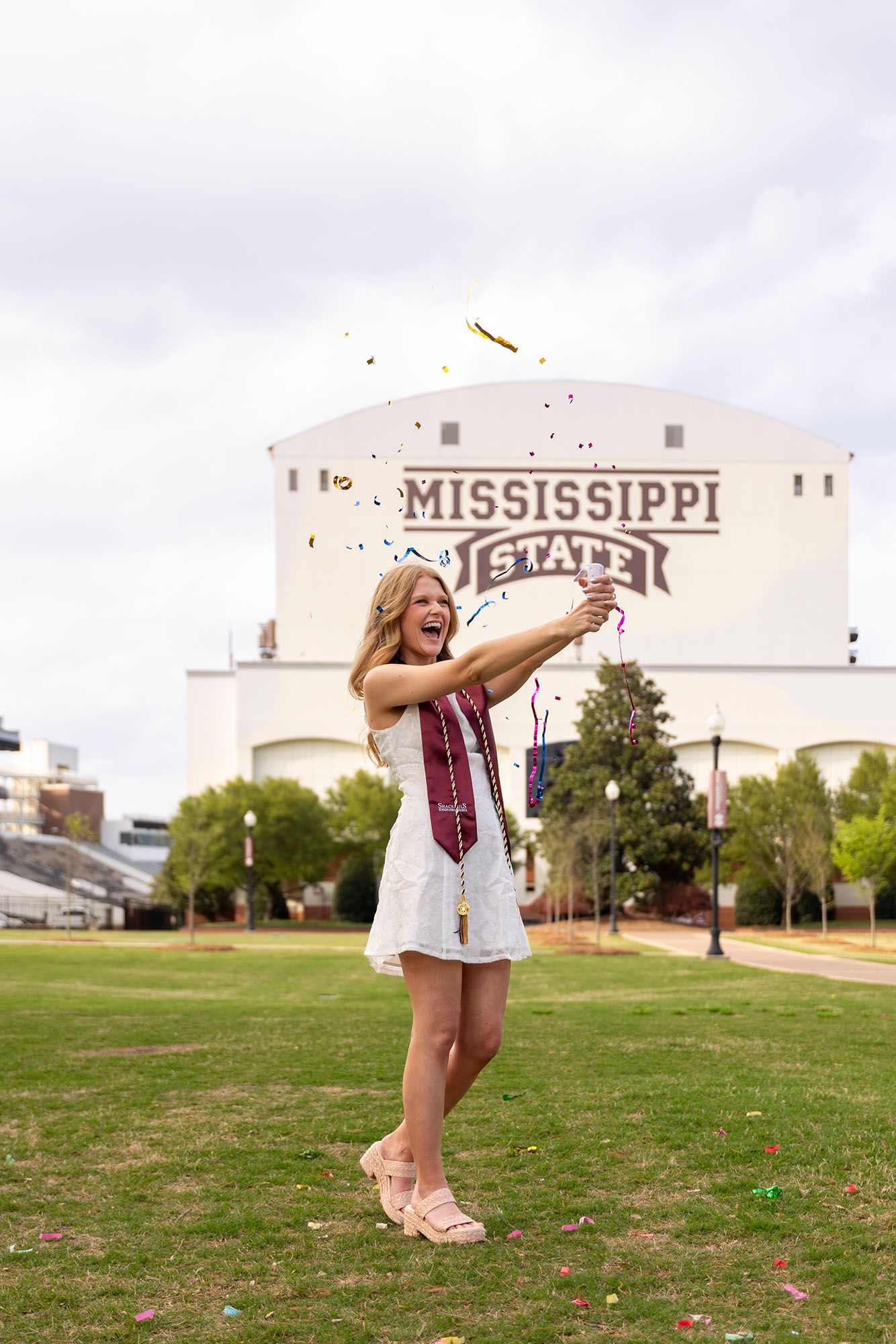 Celebrating female Mississippi State graduate pops confetti cannon on campus lawn.