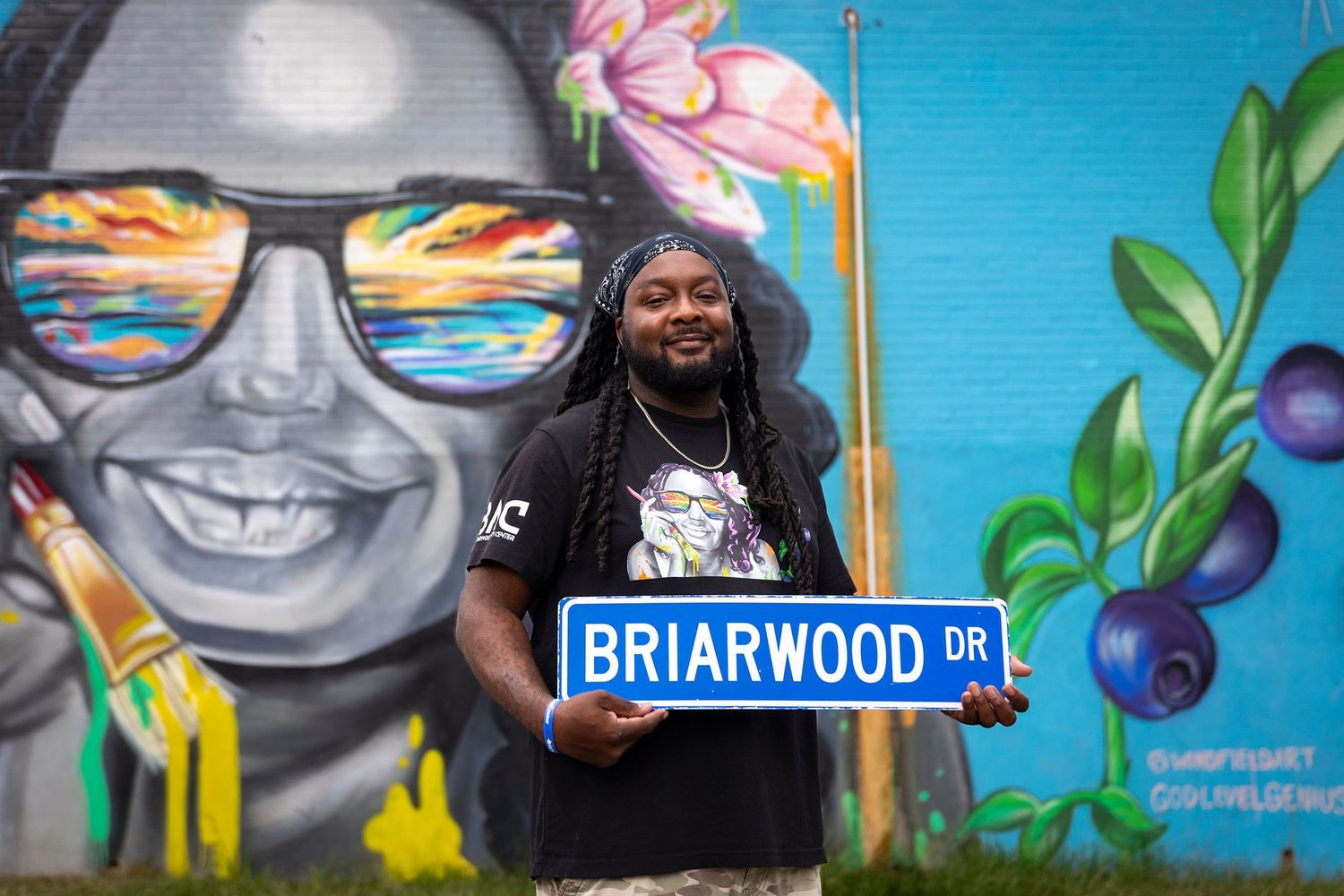 Man holding a Briarwood Drive street sign in front of a vibrant colorful mural.