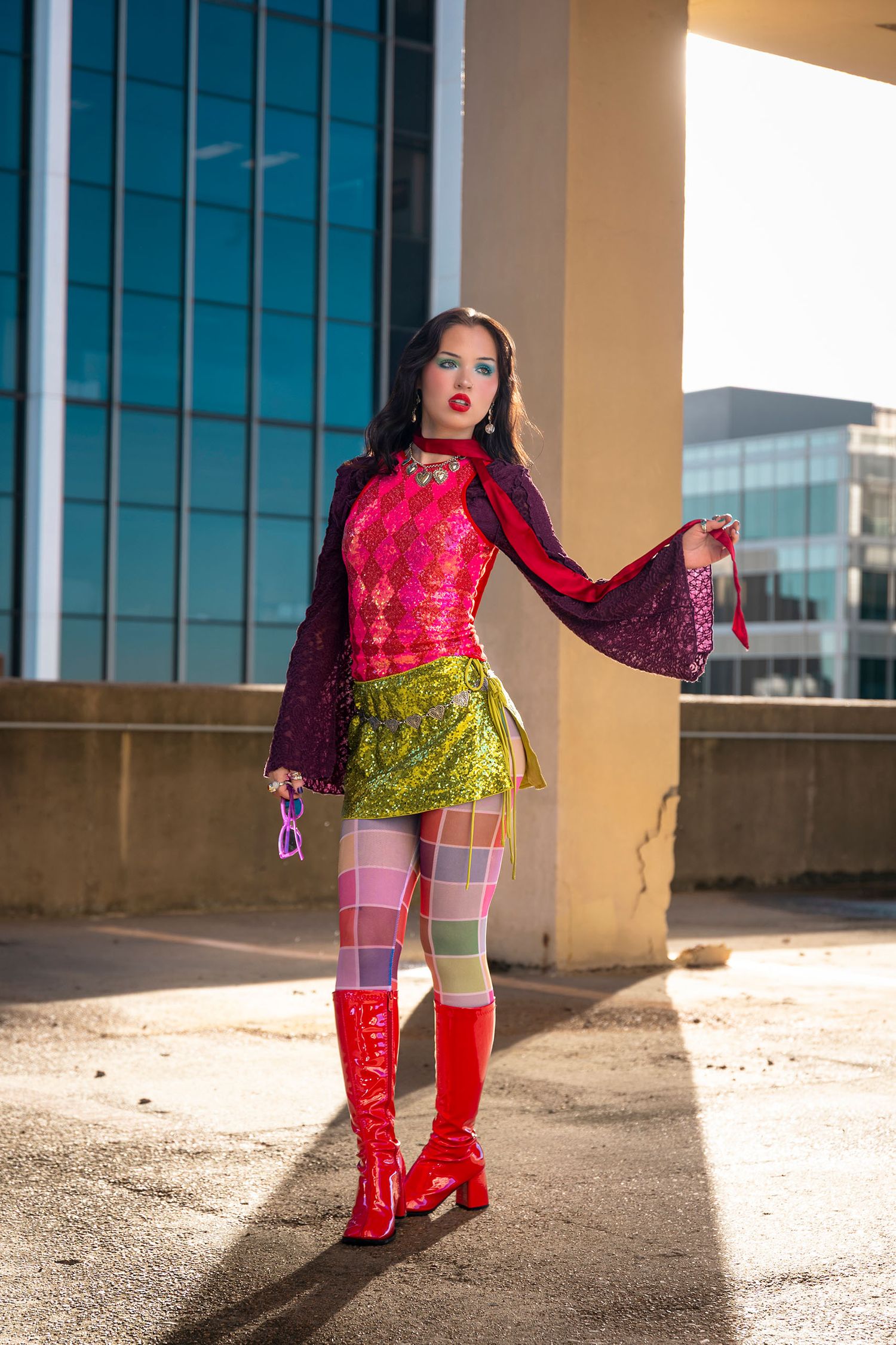 Stylish woman in vibrant pink lace top, green mini skirt, and red go-go boots posing outdoors.