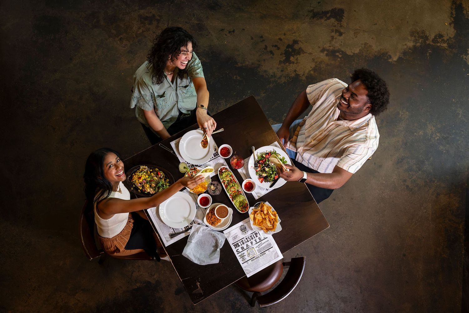 Aerial view of three friends sharing a meal at a restaurant table.