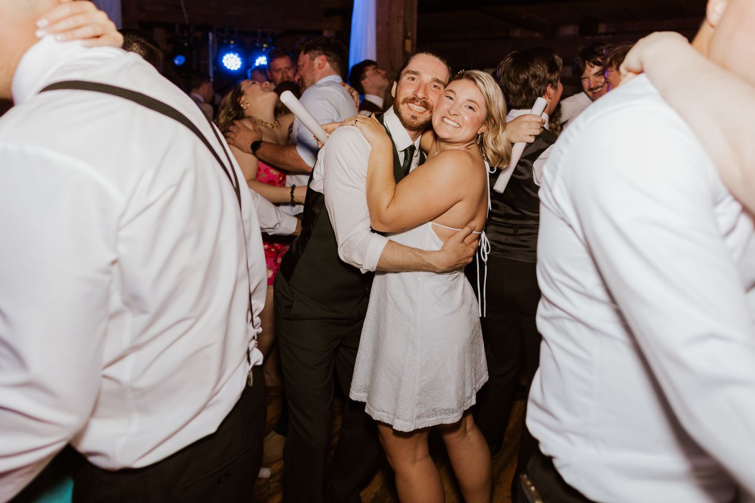 Happy couple embraces and dances together on a crowded wedding reception dance floor.