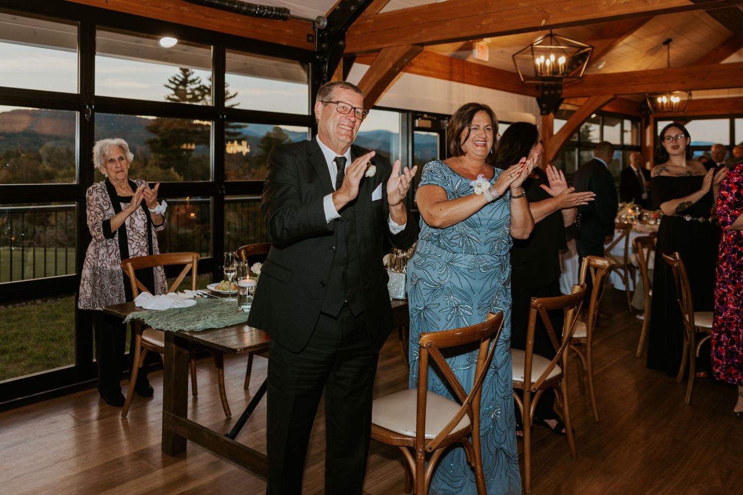 Wedding guests clapping and celebrating during reception in a rustic venue with mountain views.
