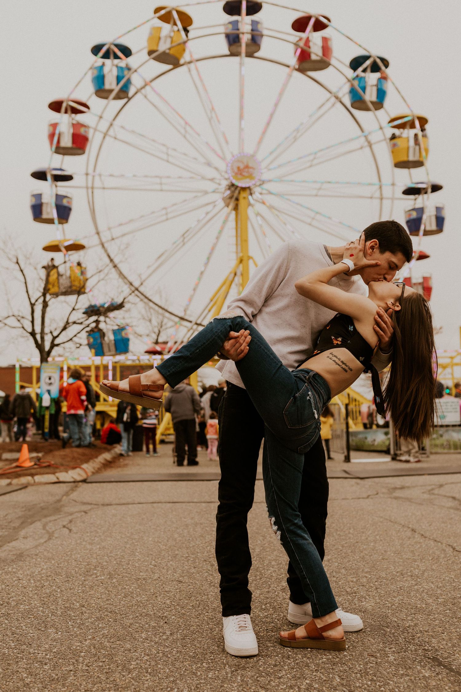 Couple showing affection while posing in front of carnival rides and attractions.