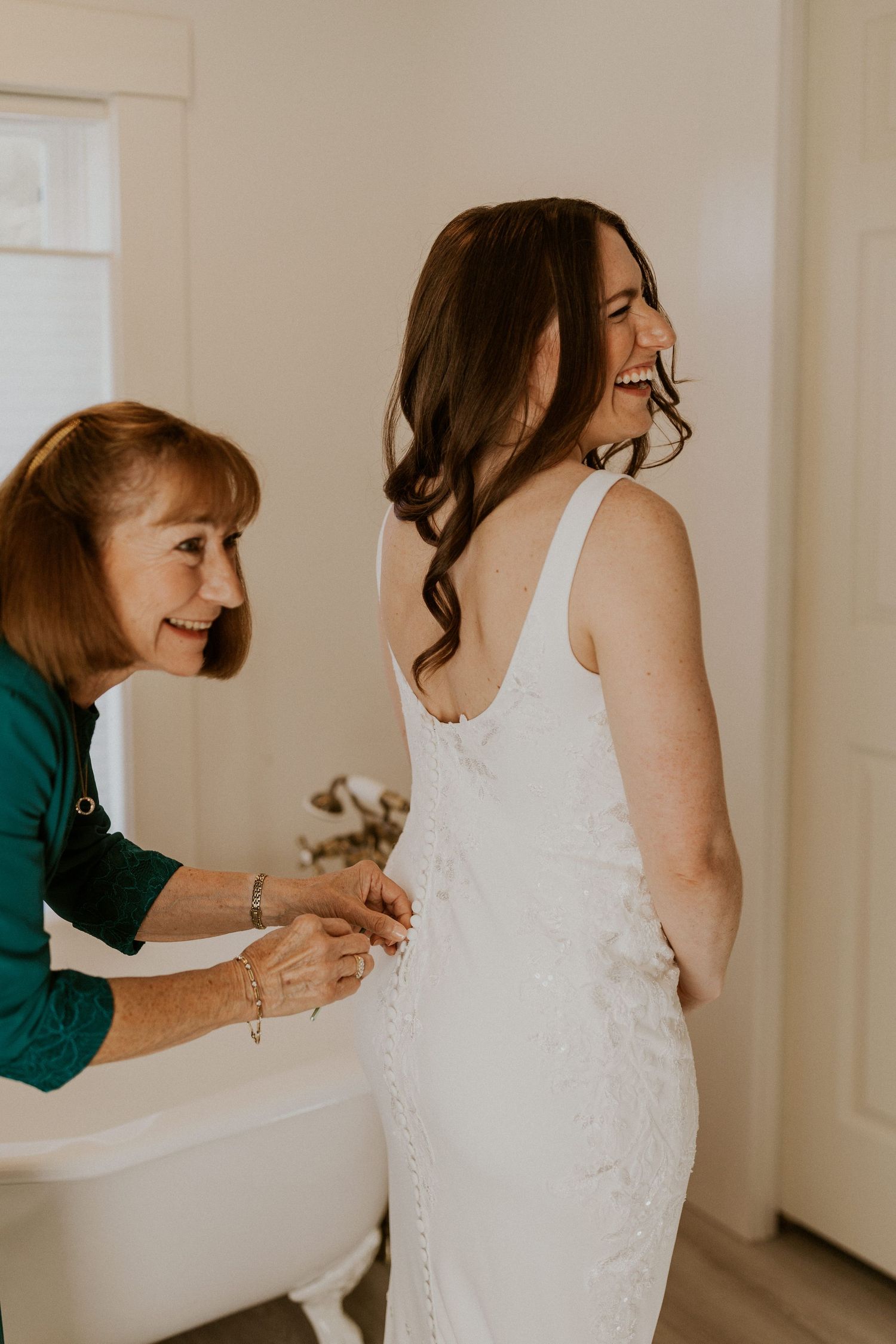 Briana's mom helping button her wedding gown while getting ready at the Woodstock Farmhouse in New Hampshire.