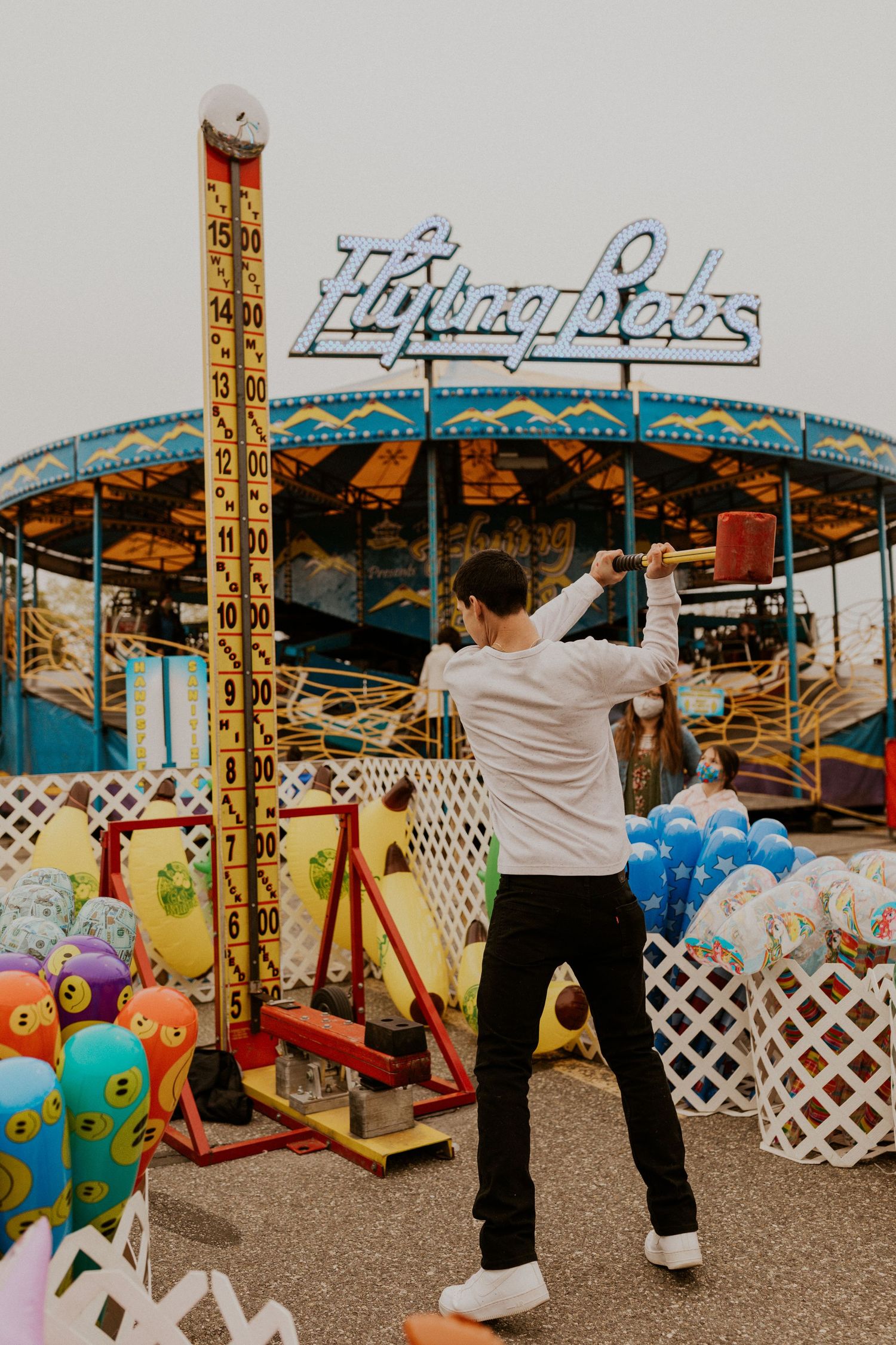 Person in white shirt posing near colorful carnival games and decorative fencing.