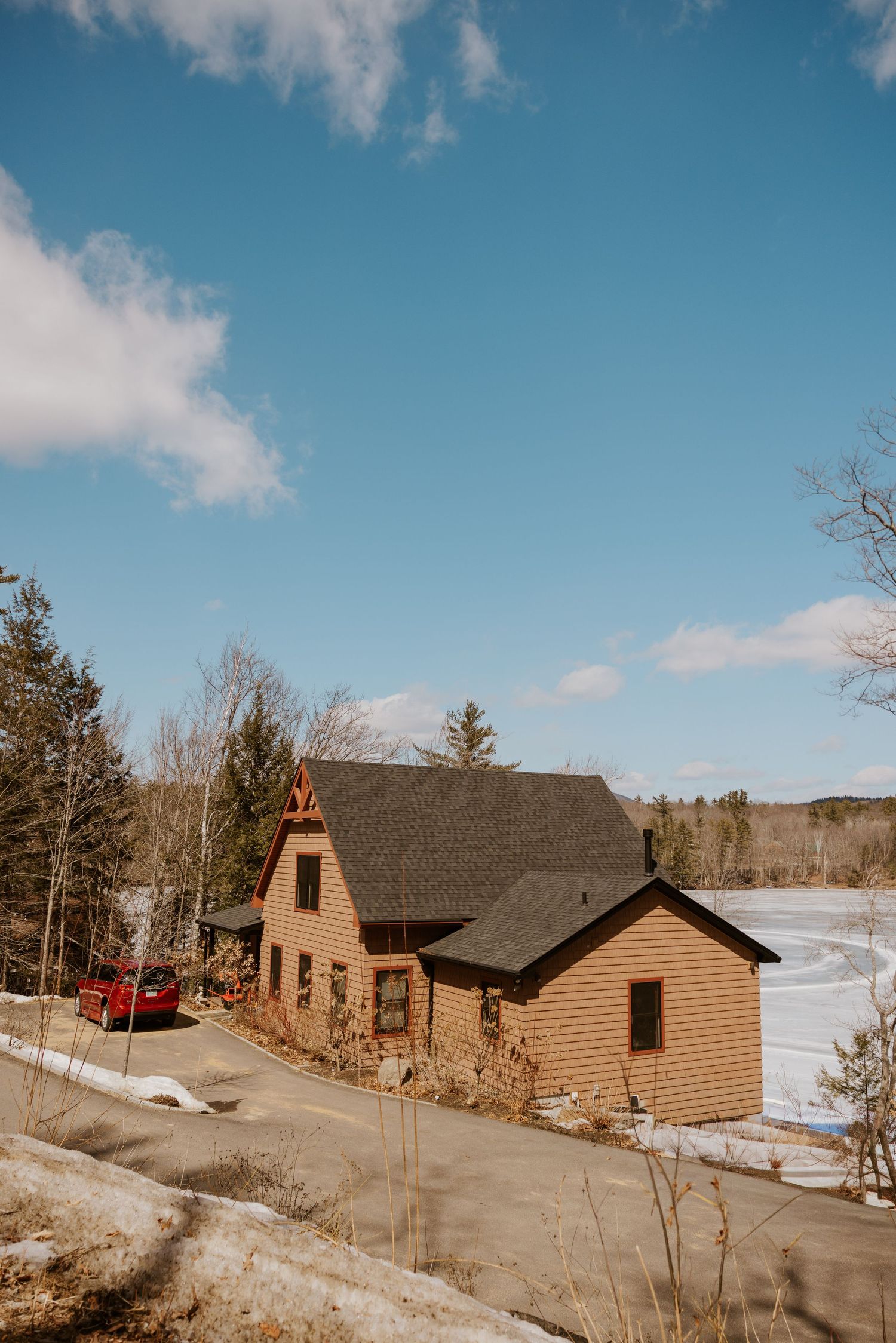 Rustic wooden cabins nestled in a snowy winter landscape with blue skies and scattered clouds overhead.