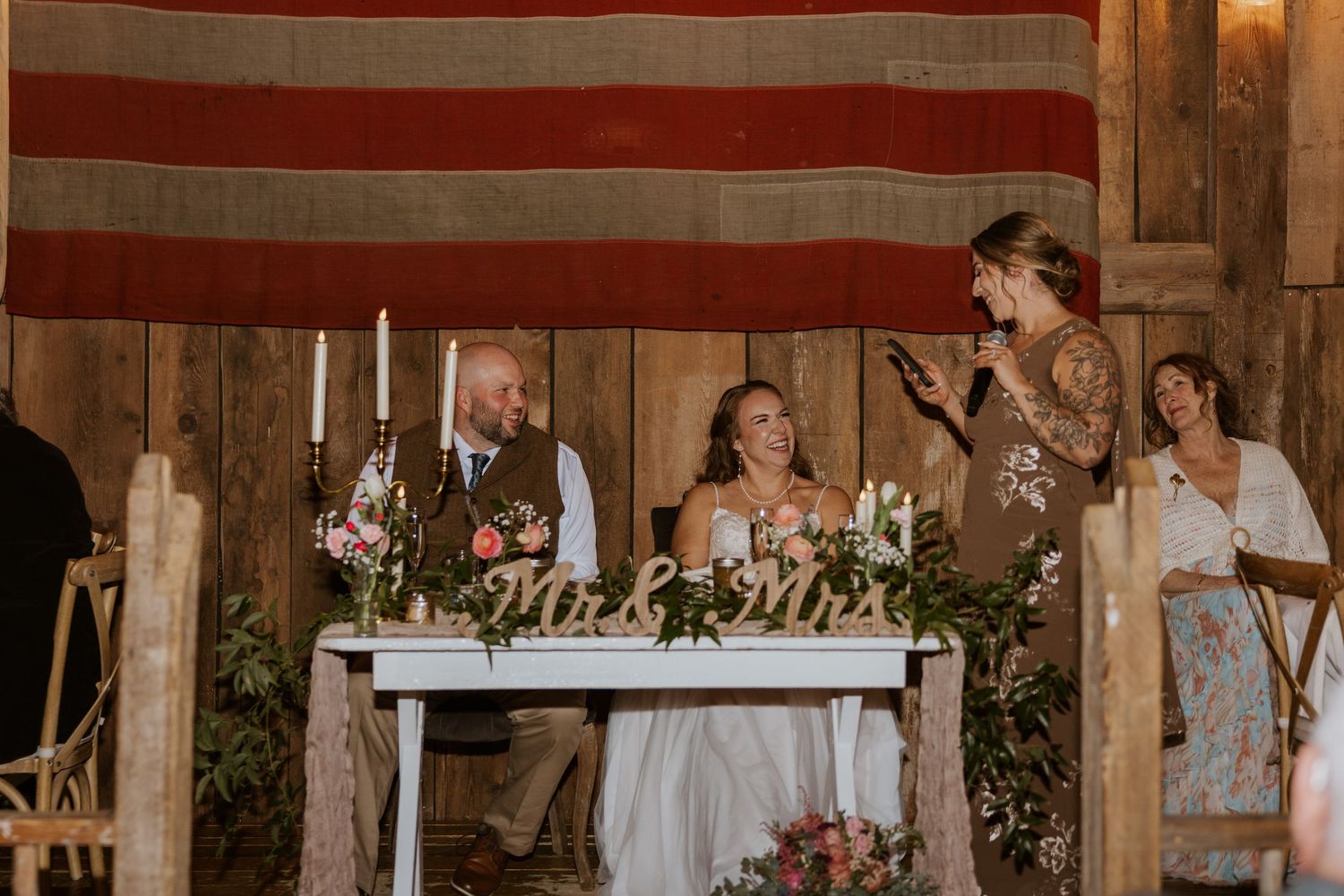 Rustic barn wedding reception setup with white tablecloths and American flag decor.