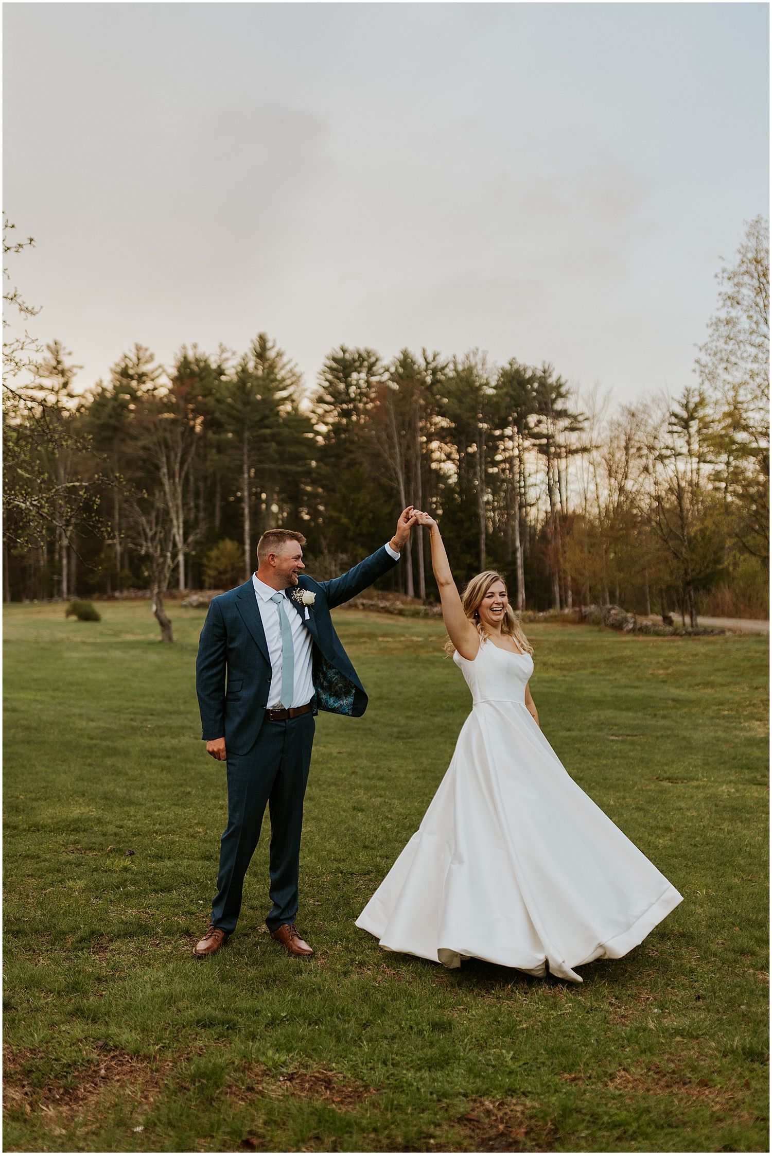 A couple celebrates joyfully in an open field with trees in the background.