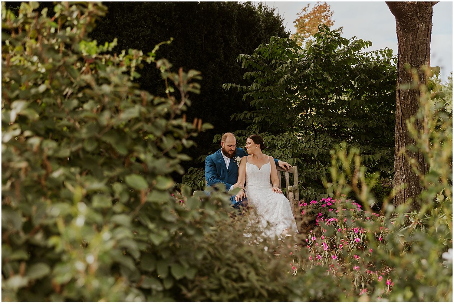 Wedding couple walking through lush garden setting with colorful flowers.