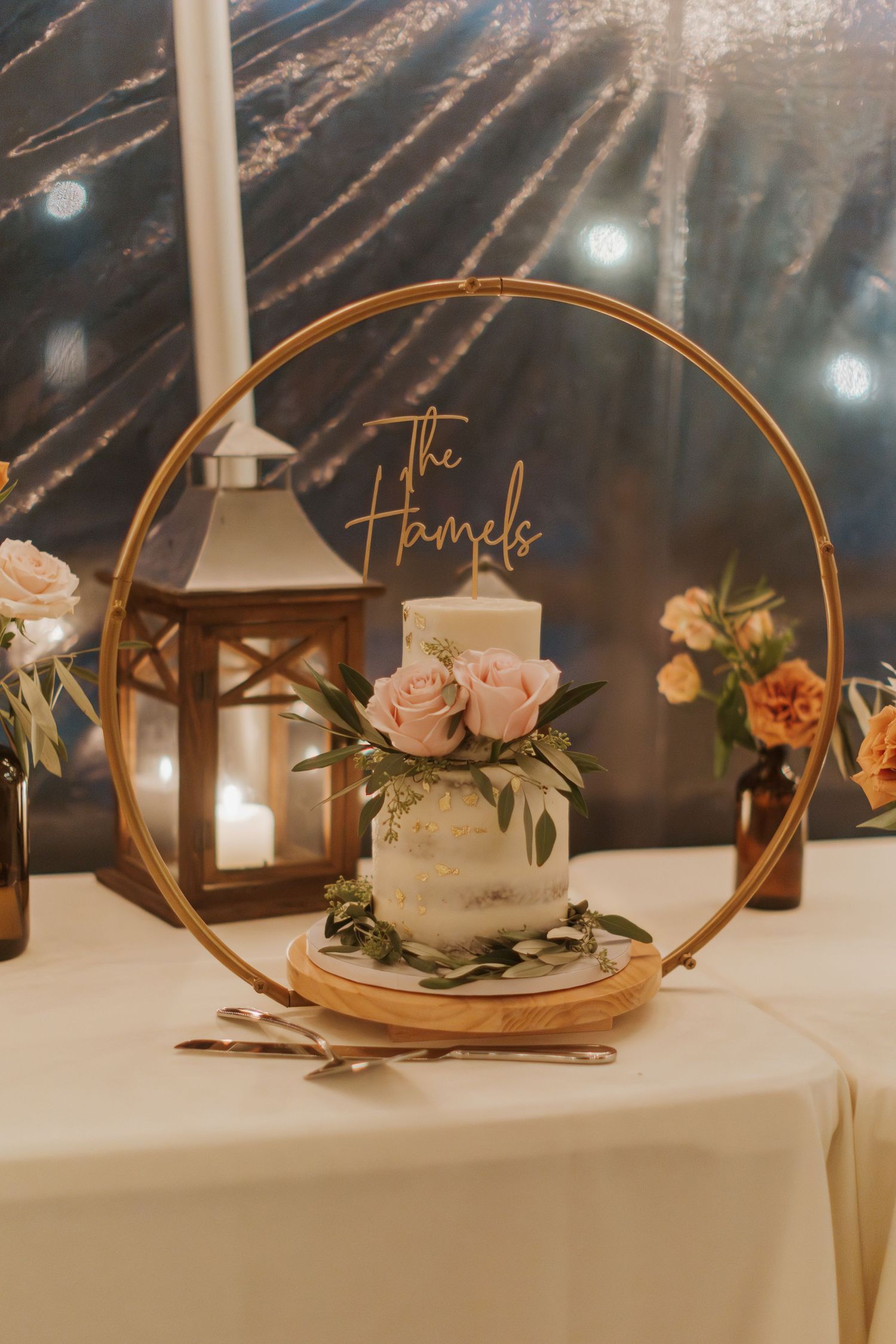 An elegant wedding table decoration featuring a gold hoop, lantern, and roses on a white tablecloth.