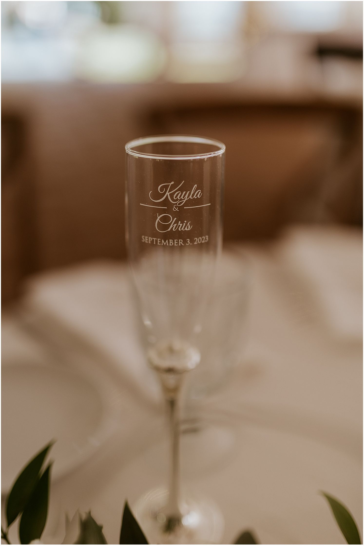 Elegant champagne flute with names Kayla and Chris engraved along with wedding date on white tablecloth.