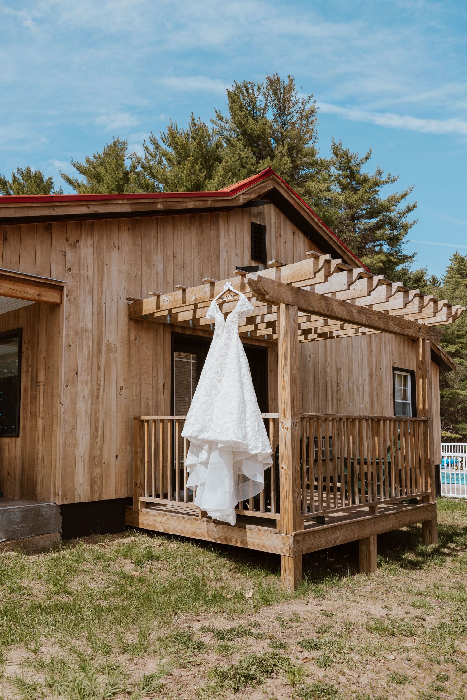 White wedding dress hanging on a wooden pergola outside a rustic cedar cabin on a sunny day.