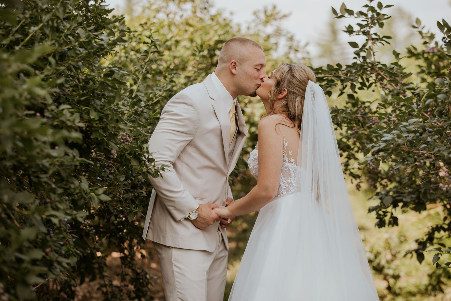 Bride and groom share a romantic kiss among lush green trees on their wedding day.