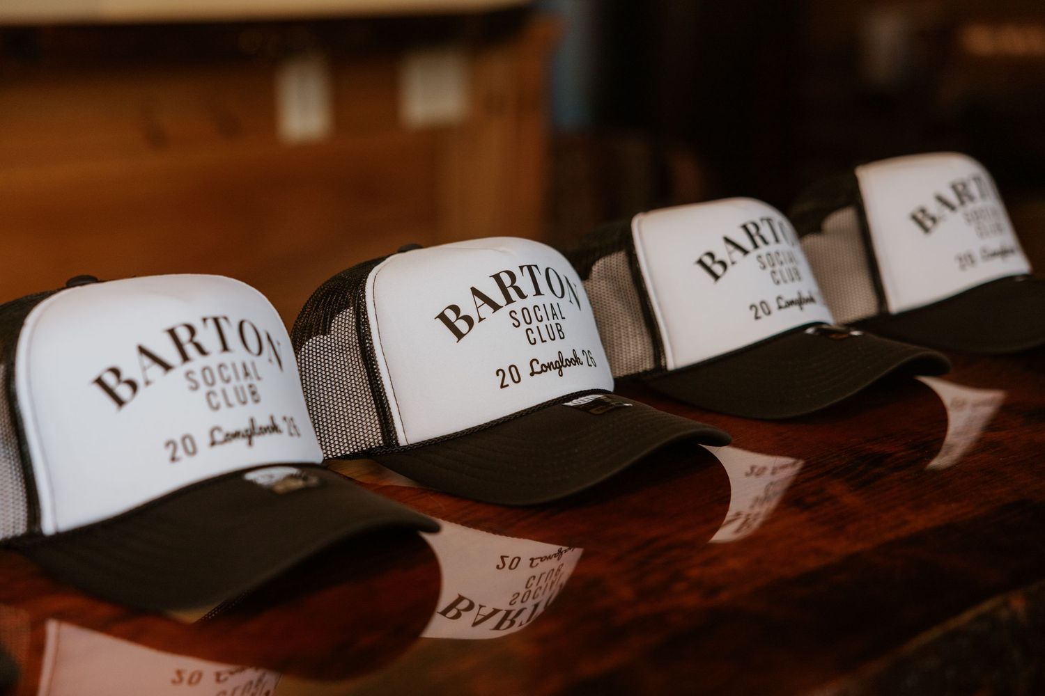 Row of Barton Social Club trucker hats displayed on a wooden shelf.