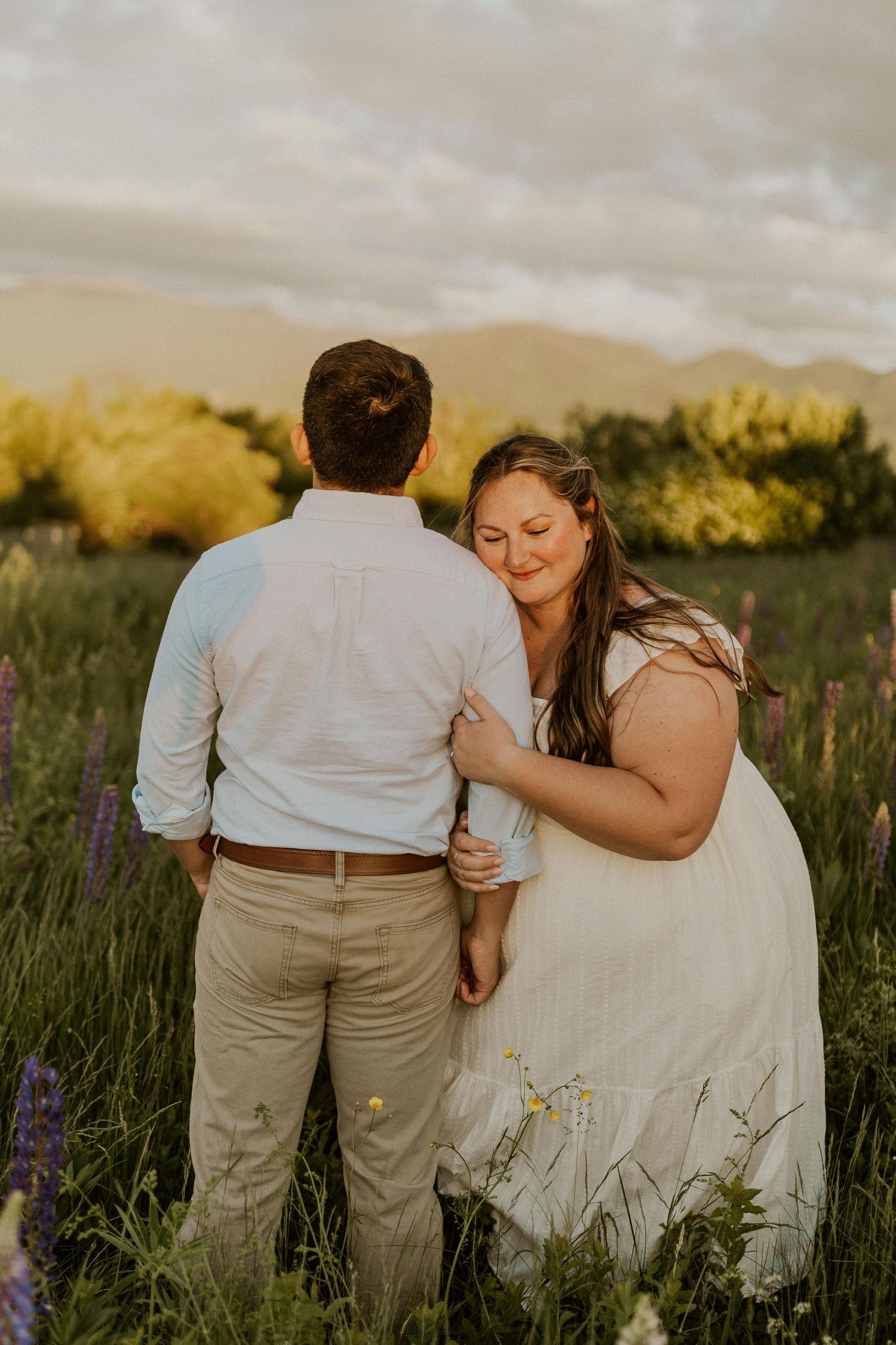 Terise hugging onto Jose's arm and smiling during an engagement photoshoot in the lupine fields of Sugar Hill NH.
