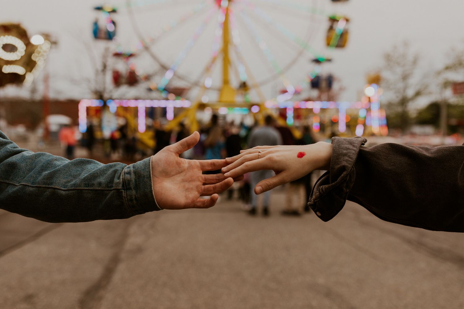 Close-up of hands reaching toward each other with carnival attractions in the background.