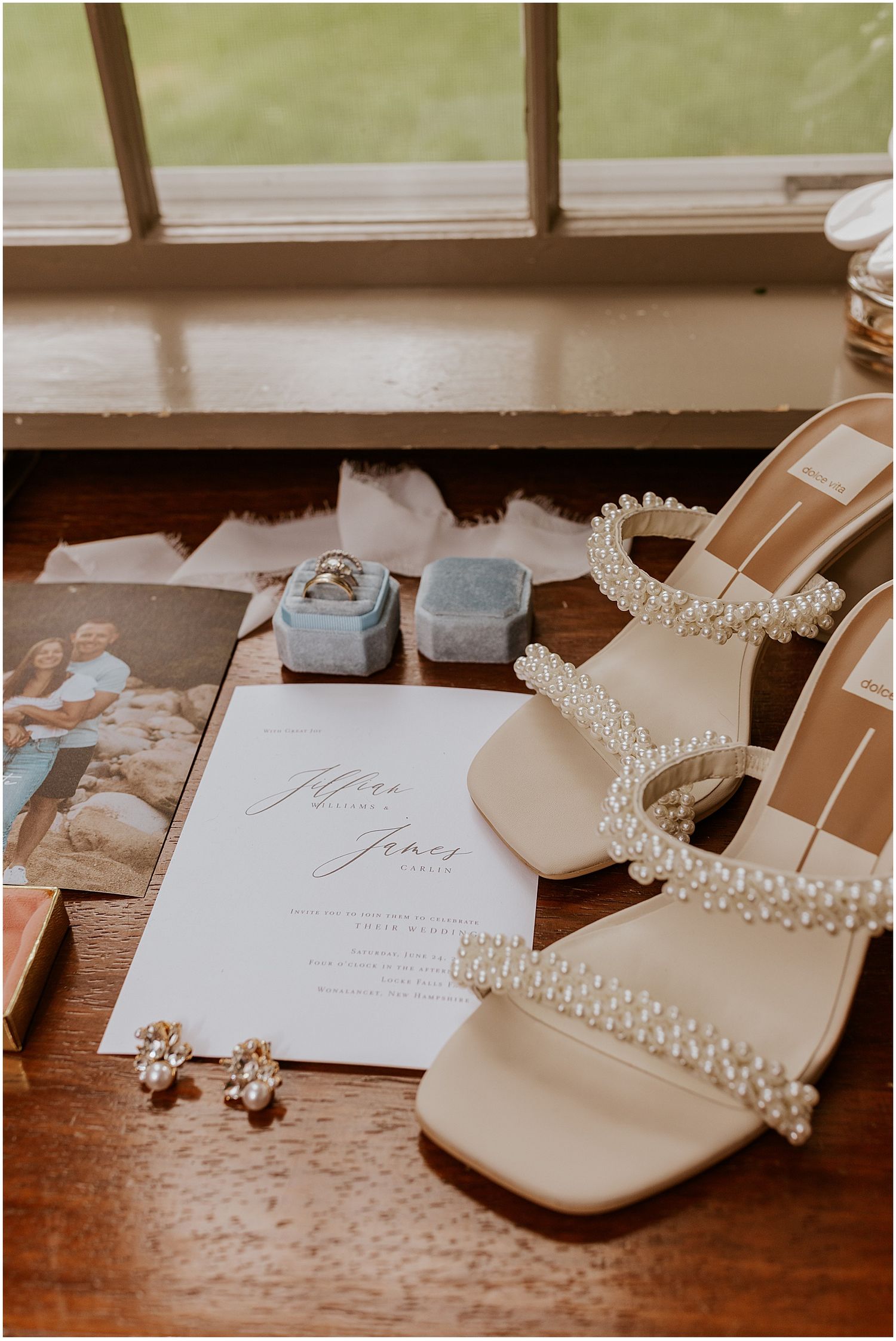 Wedding details including invitations, pearl accessories, and shoes arranged on wooden surface.