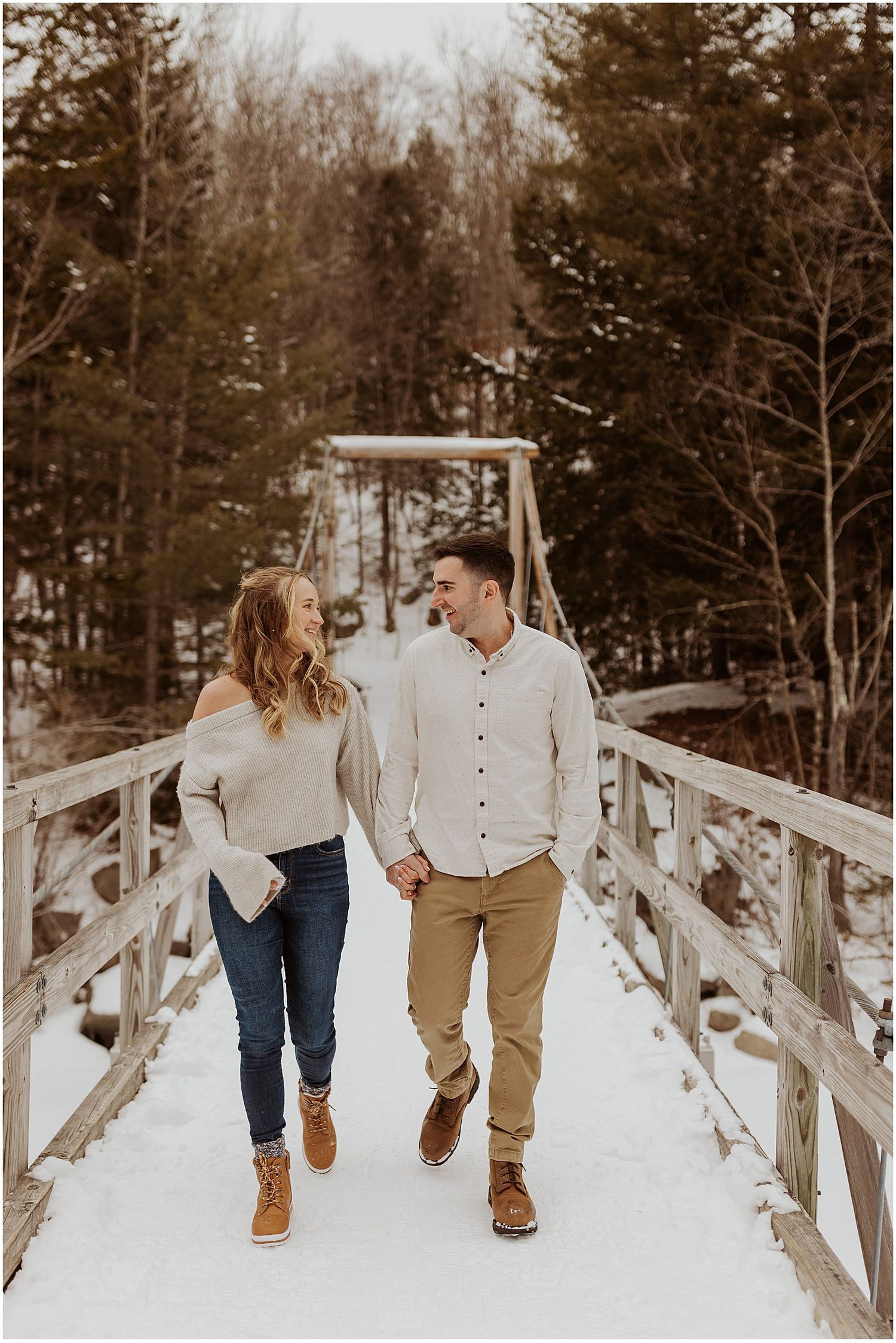 Couple walking hand in hand on a snow-covered wooden bridge in winter.