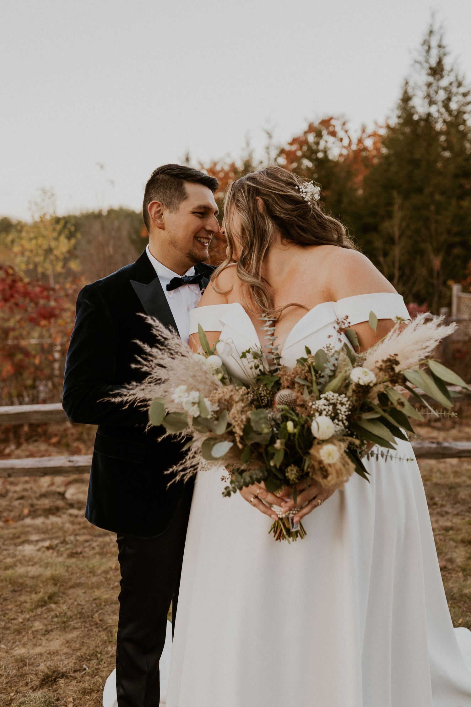 A couple embraces in formal attire holding elegant dried flower bouquets during an autumn wedding.