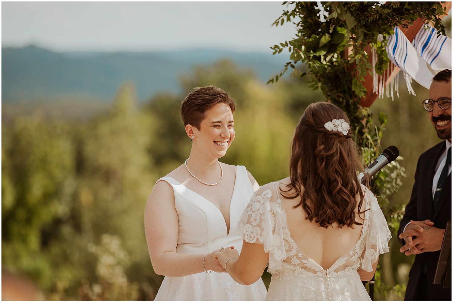 A joyful wedding celebration takes place outdoors with rolling mountains and natural scenery in the background.