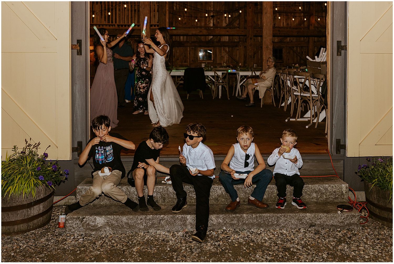 Wedding guests sitting on rustic wooden steps outside a barn venue at dusk.
