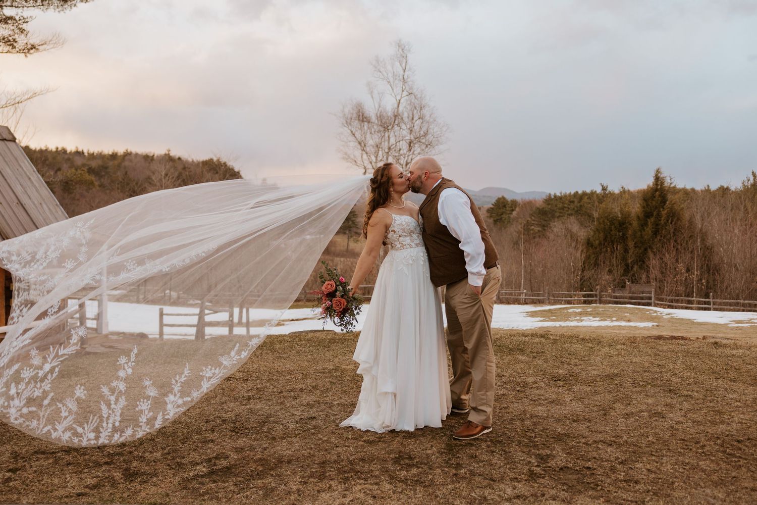 Long flowing white wedding veil blowing dramatically in the wind against a rural landscape.