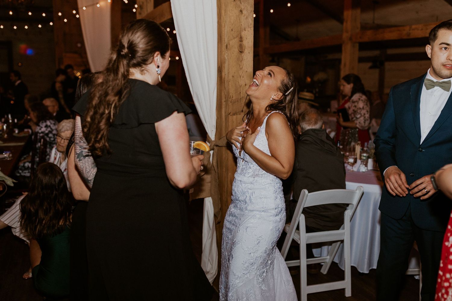 Wedding reception dance party in a dimly lit rustic barn venue with string lights.