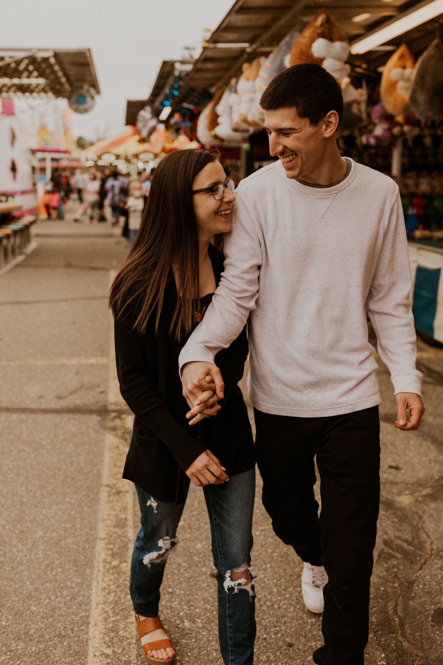 Couple walking hand in hand through a carnival midway with rides in the background.
